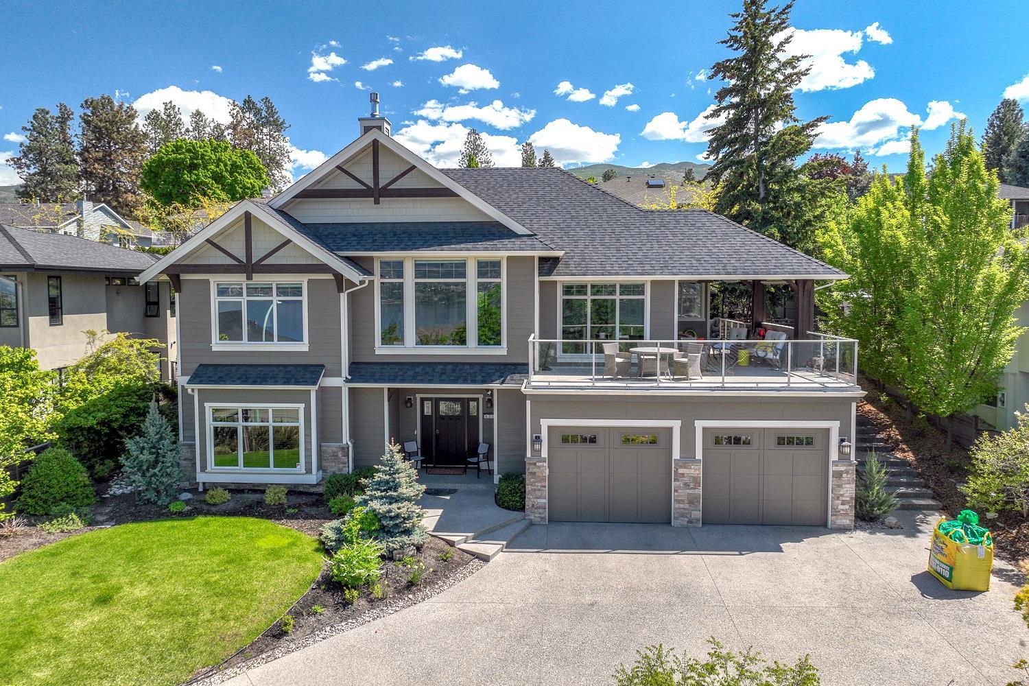 A grey craftsman-style two-storey home with a double garage, covered balcony and landscaped front yard on a sunny day.