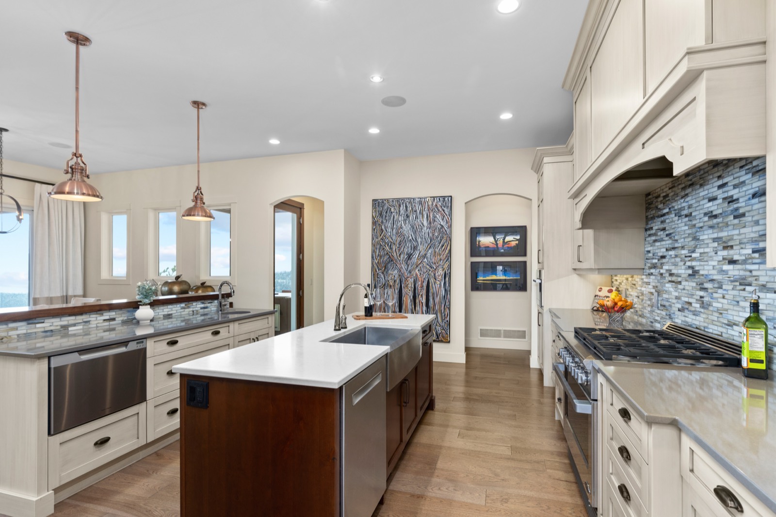 A bright kitchen with pale cabinetry, a dark wood island, stainless appliances and a glass tile backsplash.