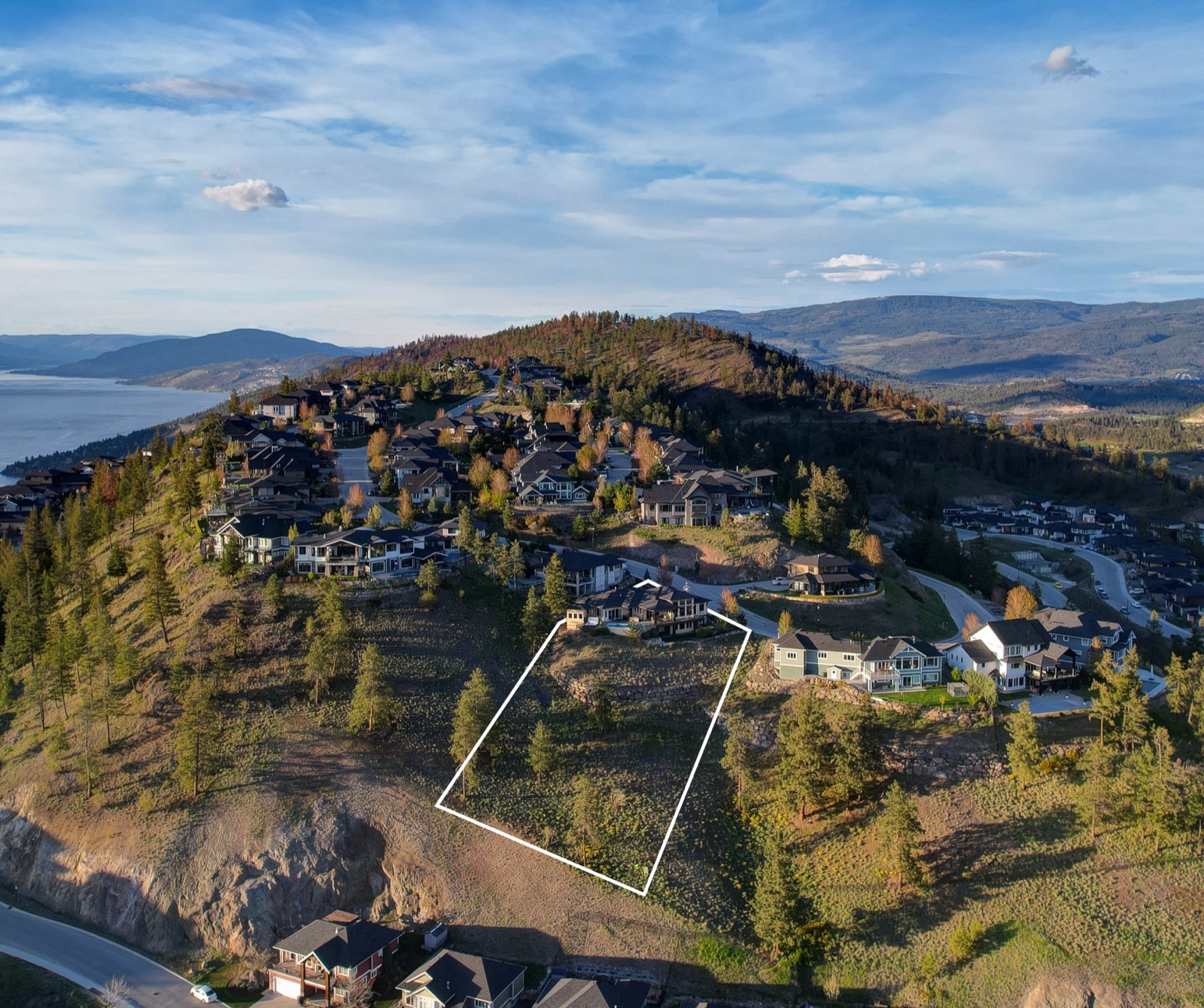 An aerial photograph of a hillside subdivision with a white outline drawn over one vacant lot to show its boundaries.